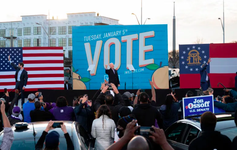 Los candidatos demócratas al Senado Jon Ossoff (L), Raphael Warnock (R) y el Presidente electo Joe Biden (C) saludan desde el escenario.