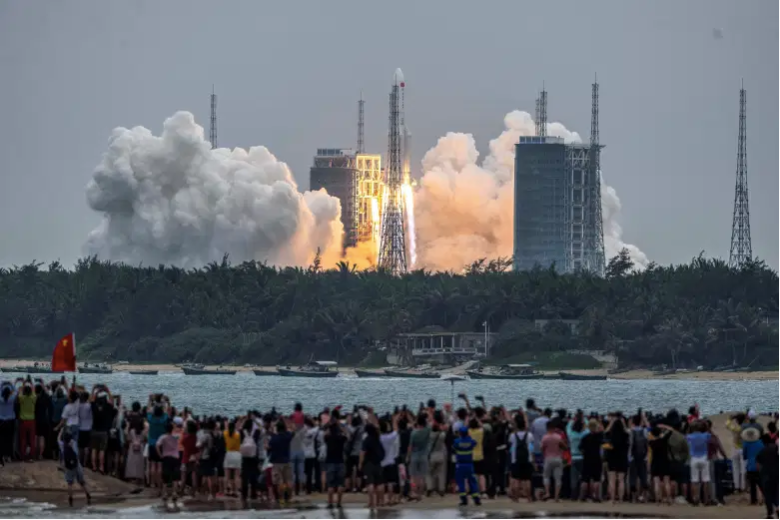 La gente observa un cohete Long March 5B, que transporta el módulo central de la estación espacial Tianhe de China, mientras despega del Centro de Lanzamiento Espacial Wenchang en la provincia de Hainan, en el sur de China, el 29 de abril de 2021.