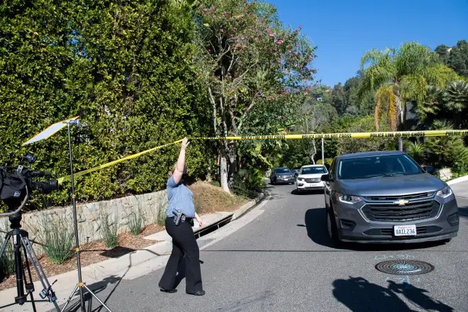 Un oficial de policía cruza debajo de la cinta policial mientras los miembros de los medios de comunicación se reúnen cerca de la cuadra 1100 de Maytor Place, donde se encuentra la casa de Jacqueline Avant en la cima de la colina, en Beverly Hills, California, el 1 de diciembre de 2021. -